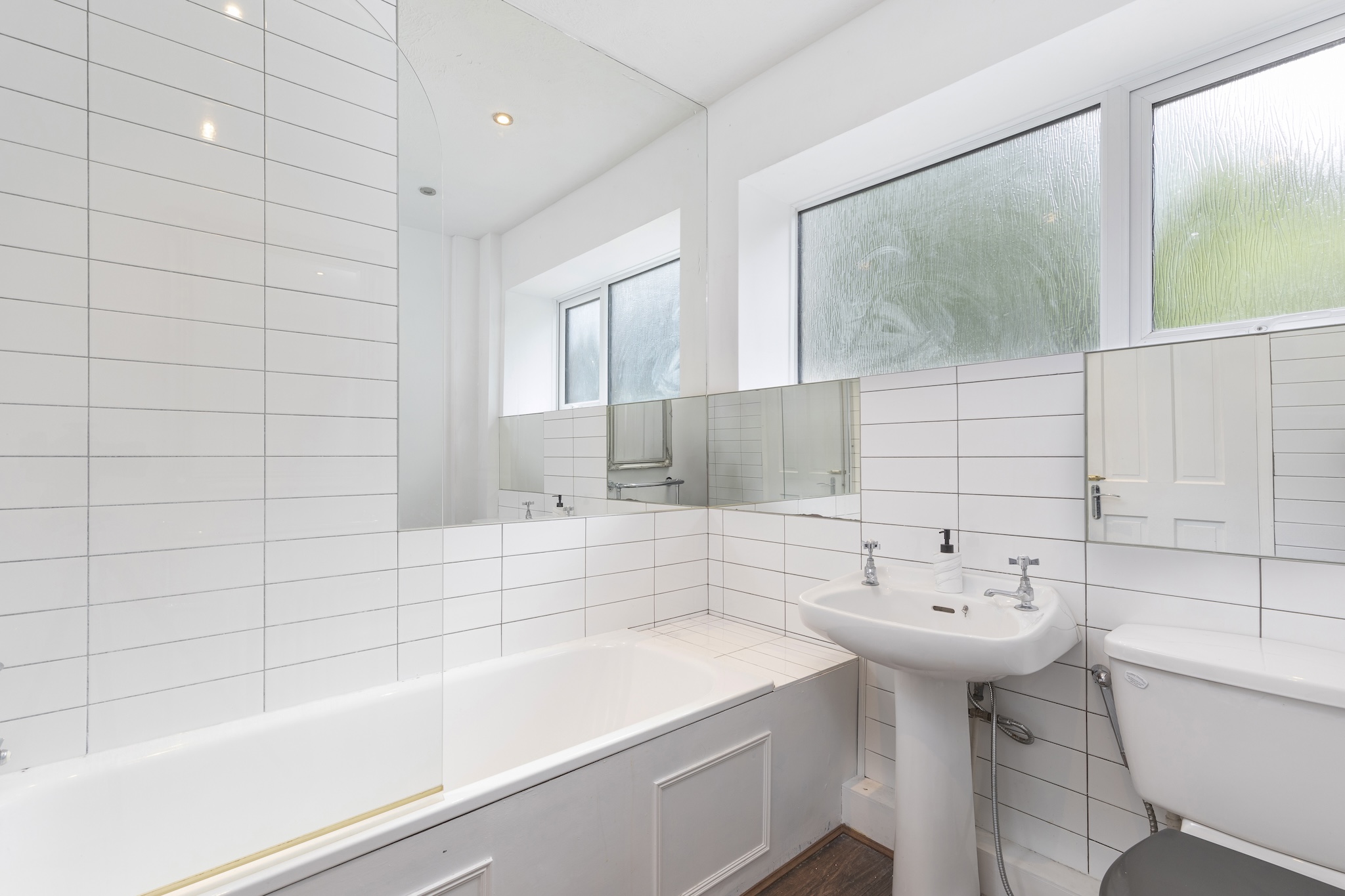 Bright white-tiled bathroom with bath, shower and frosted windows