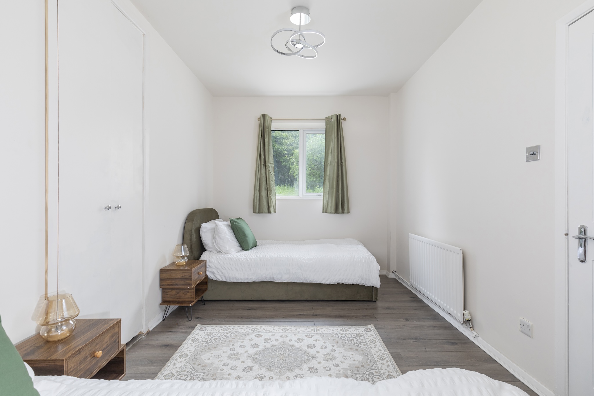 Twin bedroom with sage velvet headboards and soft natural light